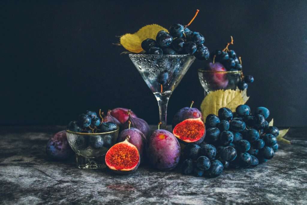 Dark moody still life of fresh grapes and figs in a glass setting, highlighting autumn flavors.